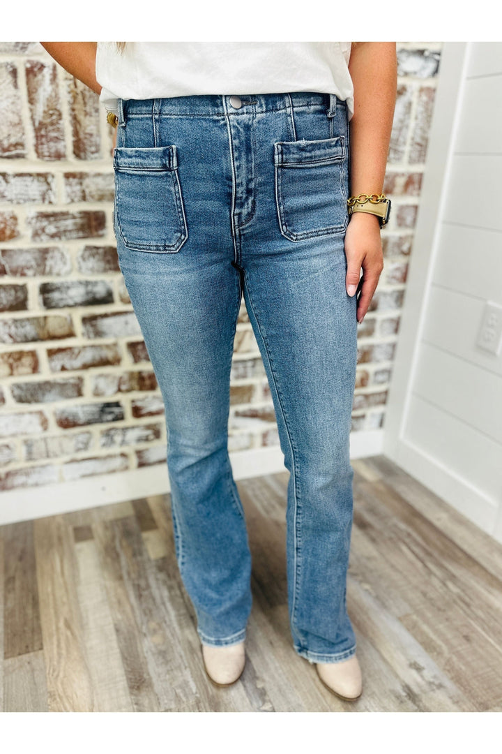 Woman wearing high rise front pocket detail flare jeans against a brick wall.