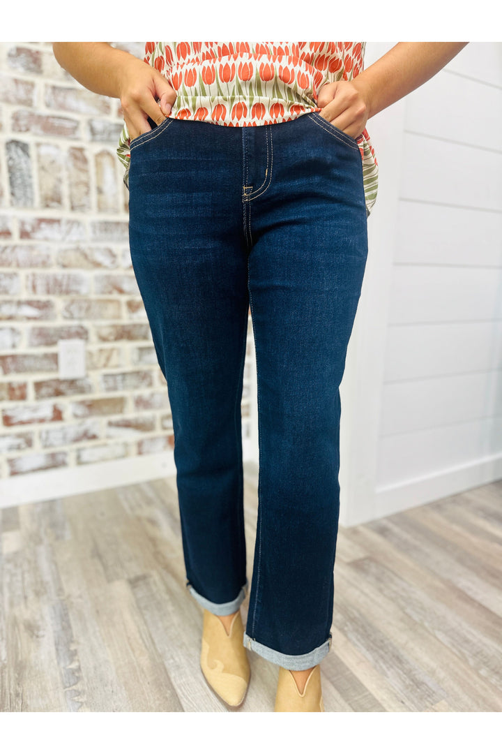 Woman wearing dark high rise crop straigh jeans with cuff at the bottom standing against a brick wall.