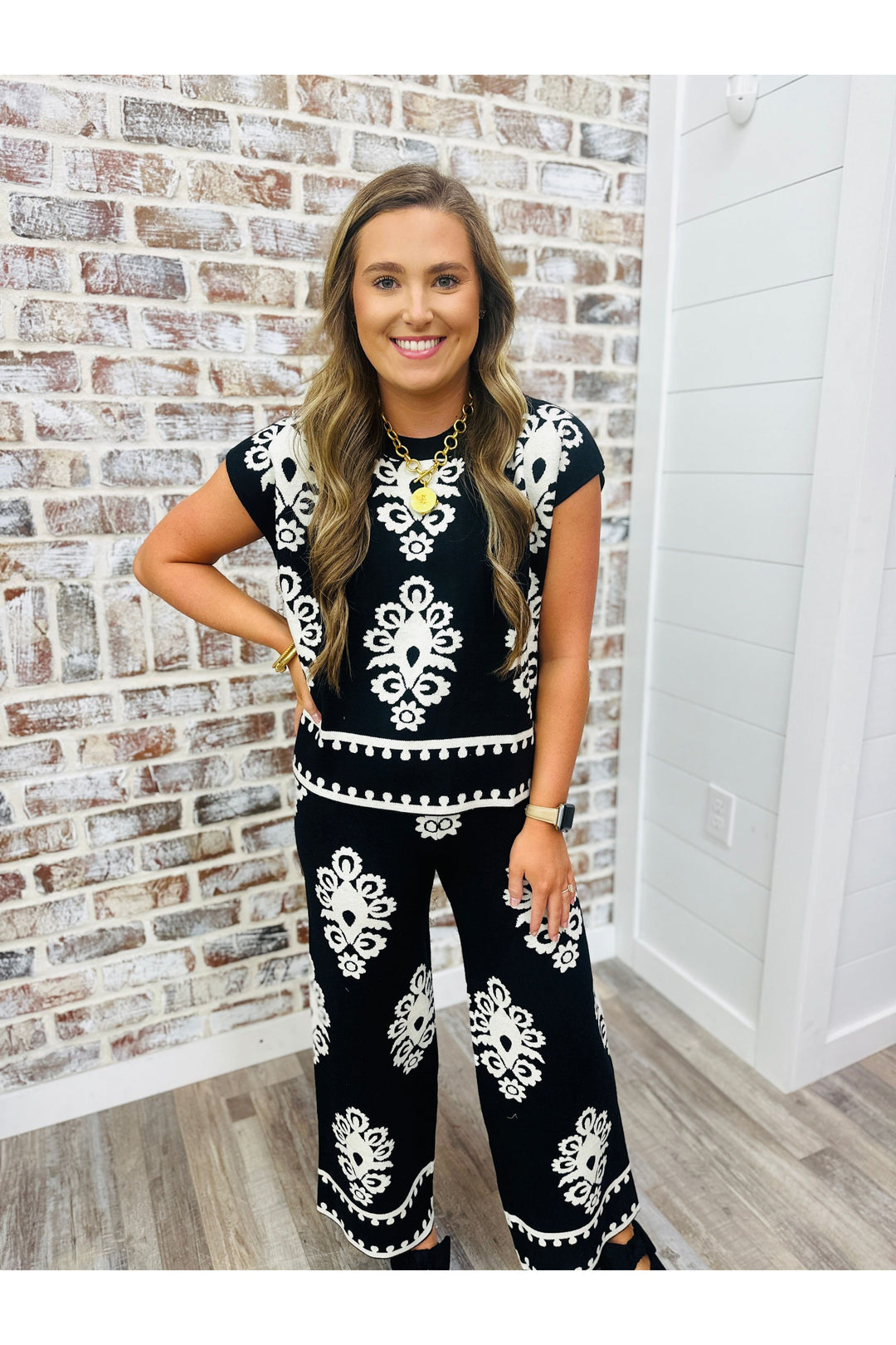 Woman wearing black and white design pants set standing against a brick wall.