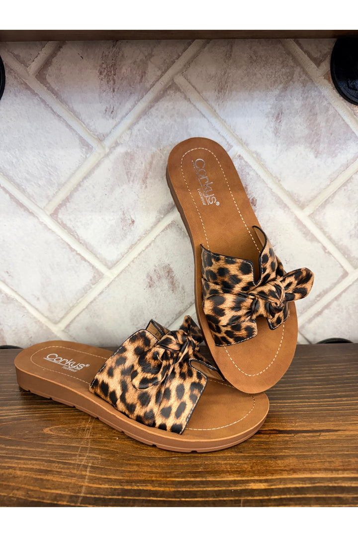 Pair of leopard print sandals on a tiled floor and wooden surface.