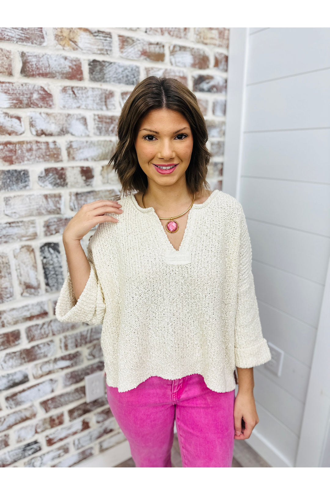 Woman wearing ivory knit sweater paired with pink pants and necklace 