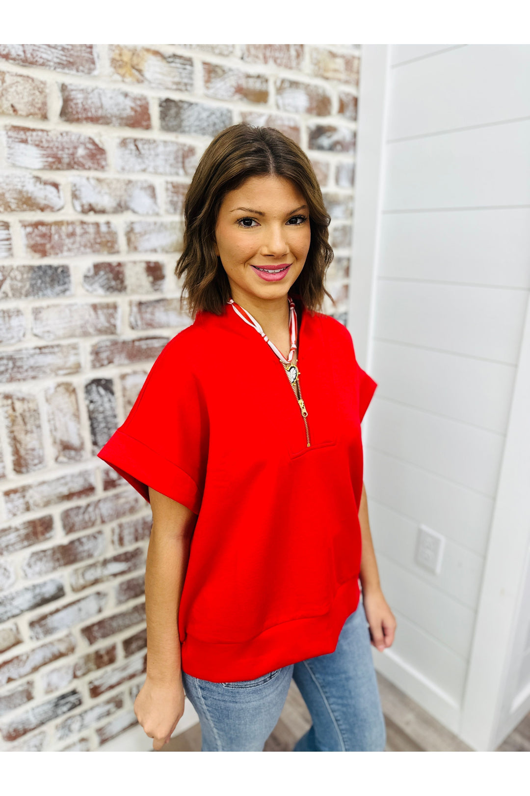 Women wearing red top with gold zipper standing against a brick wall.
