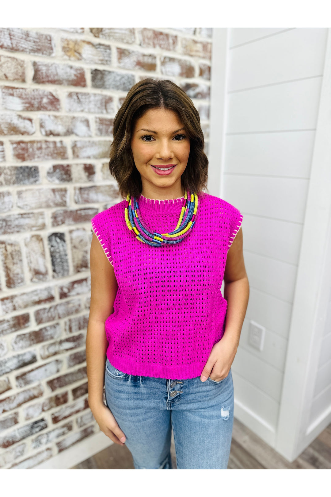 Woman wearing magenta sweater top with white stitch detail.