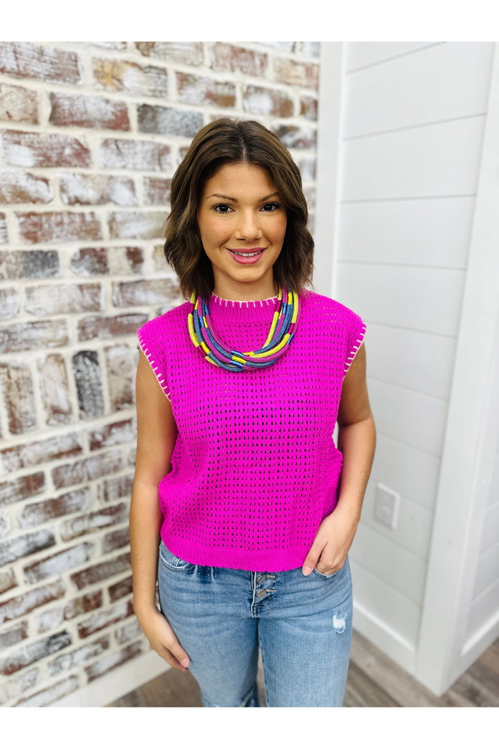 Woman wearing magenta sweater top with white stitch detail.