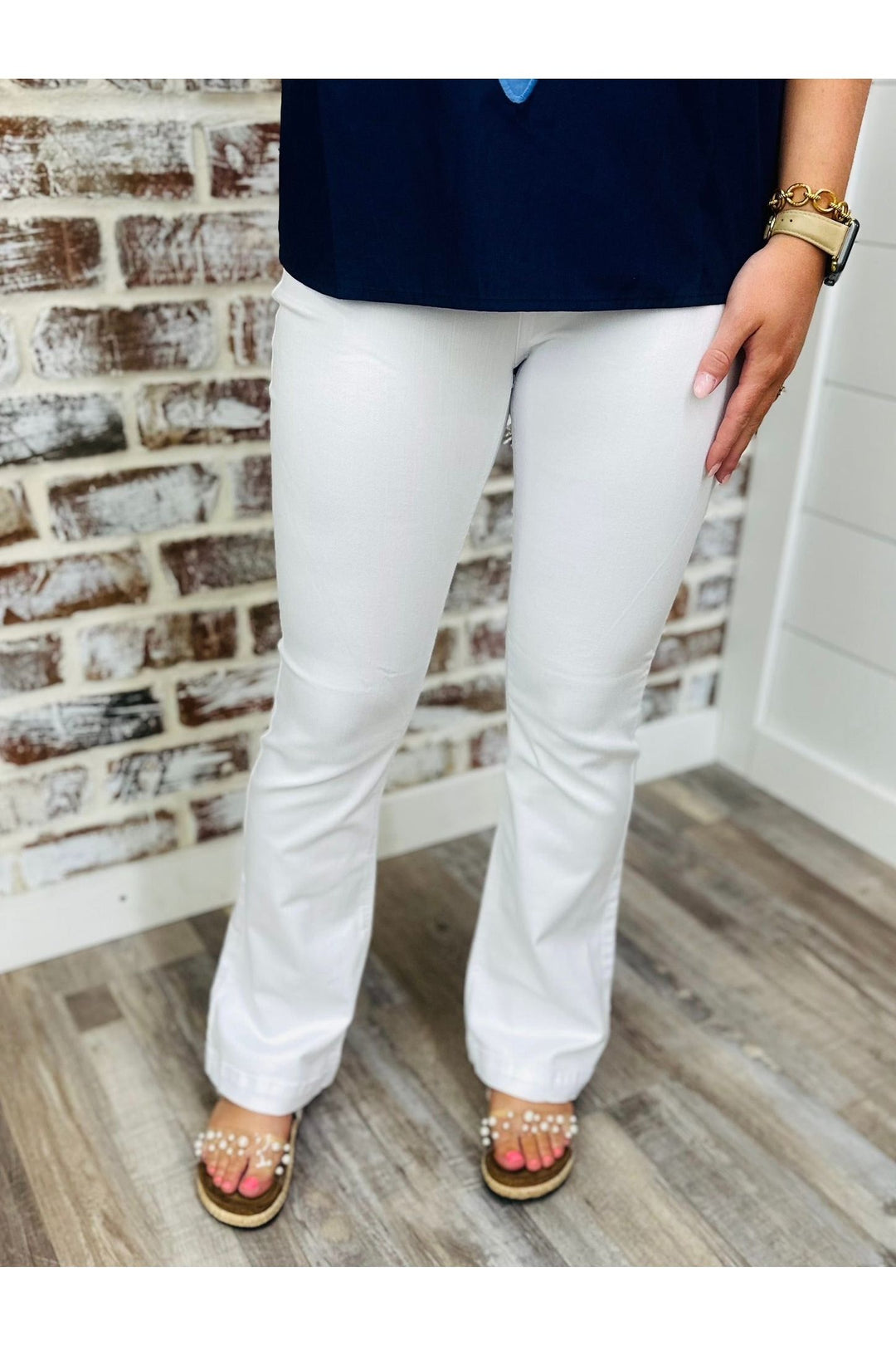 Woman wearing petite white flares with pearl sandals standing against a brick wall.