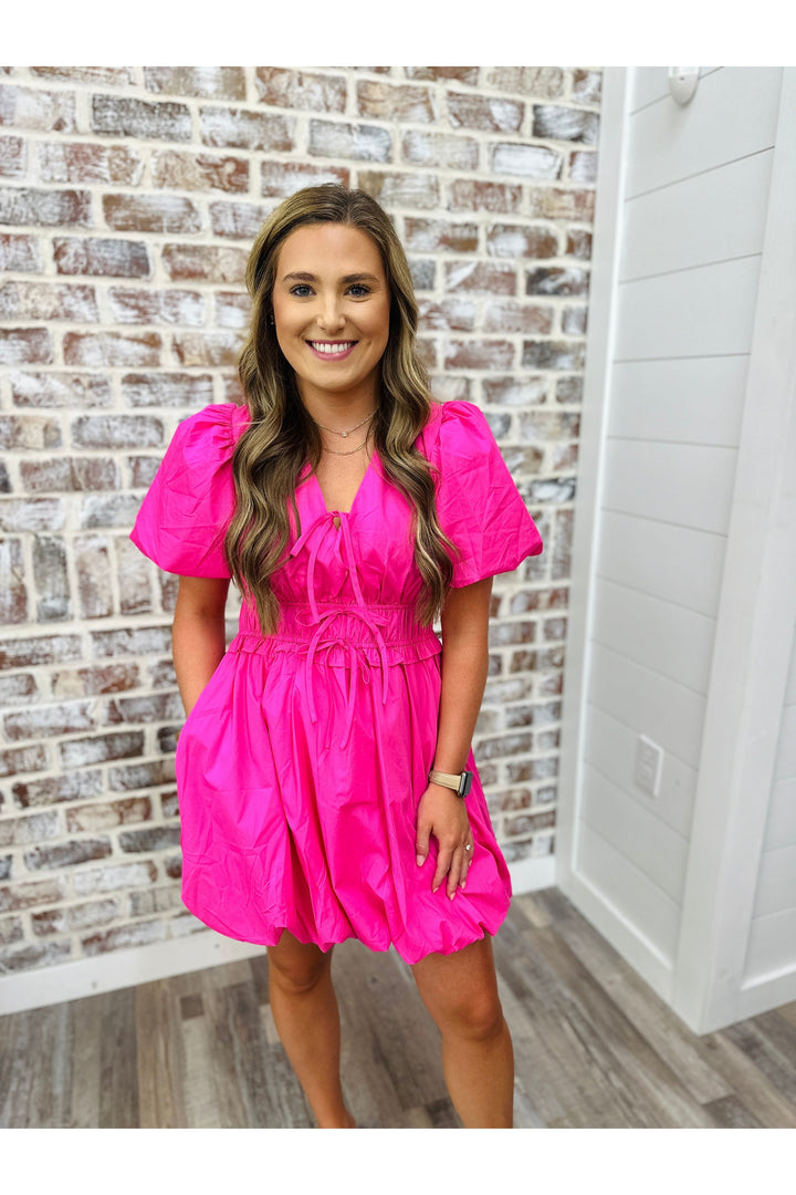short sleeve pink dress above the knee, bow tie details down the front, sinched waist and bubble skirt
