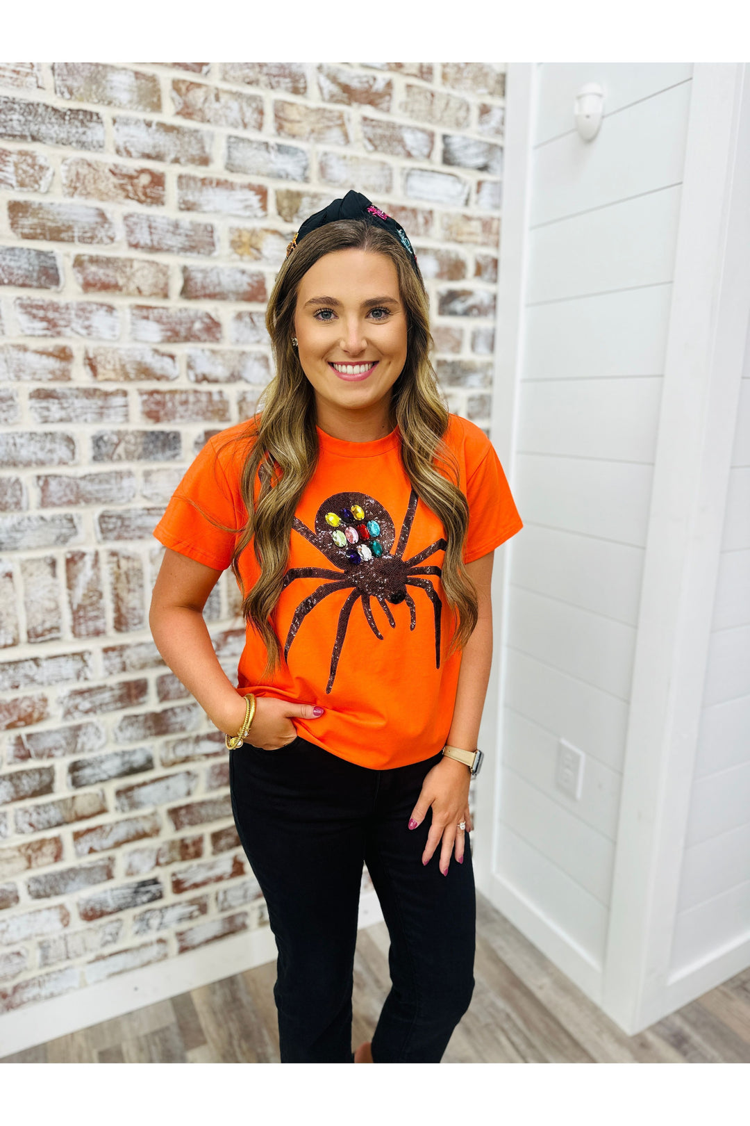 Woman wearing orange shirt with a jeweled spider on it 
