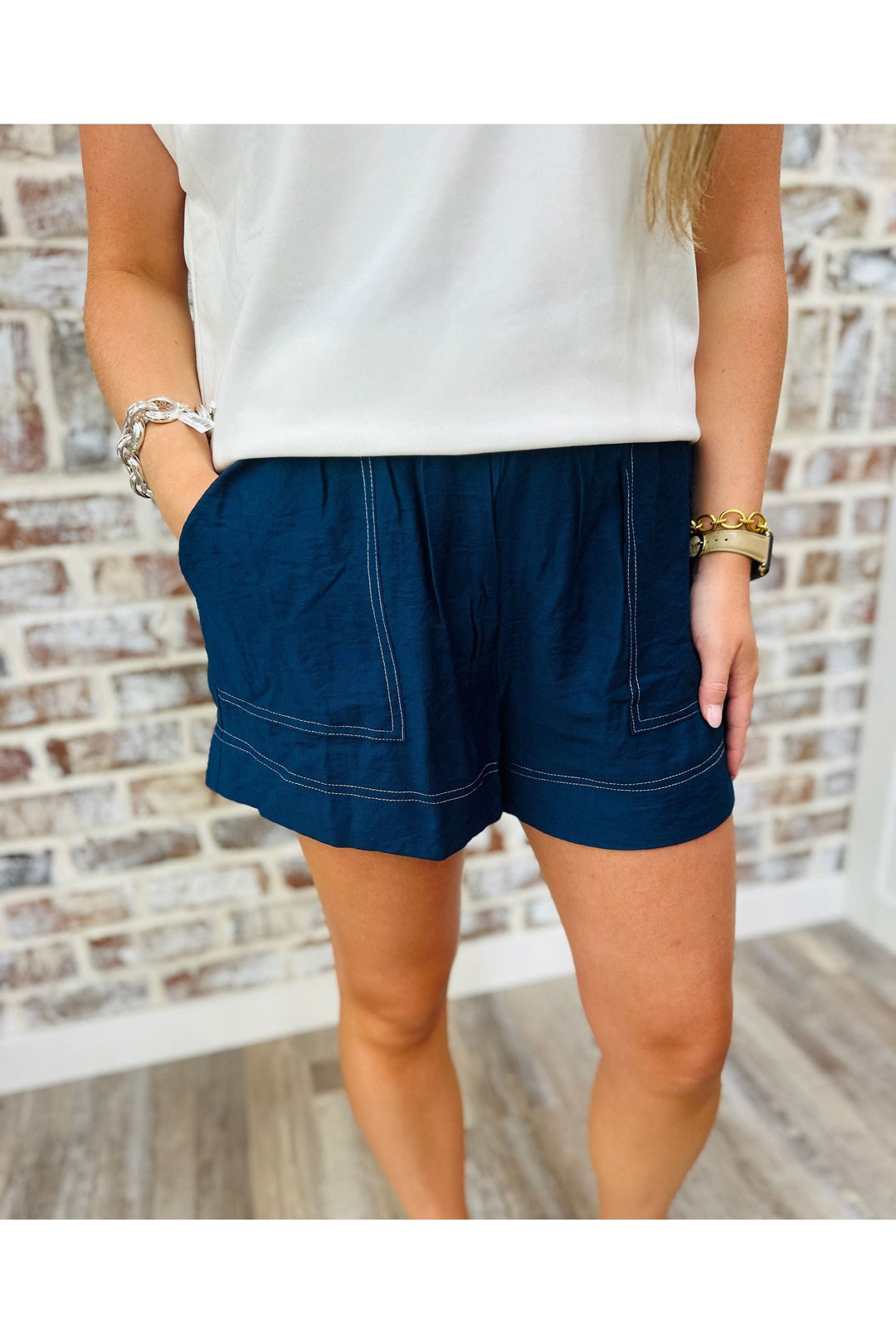 Woman wearing navy shorts with white stitching standing against a brick wall.