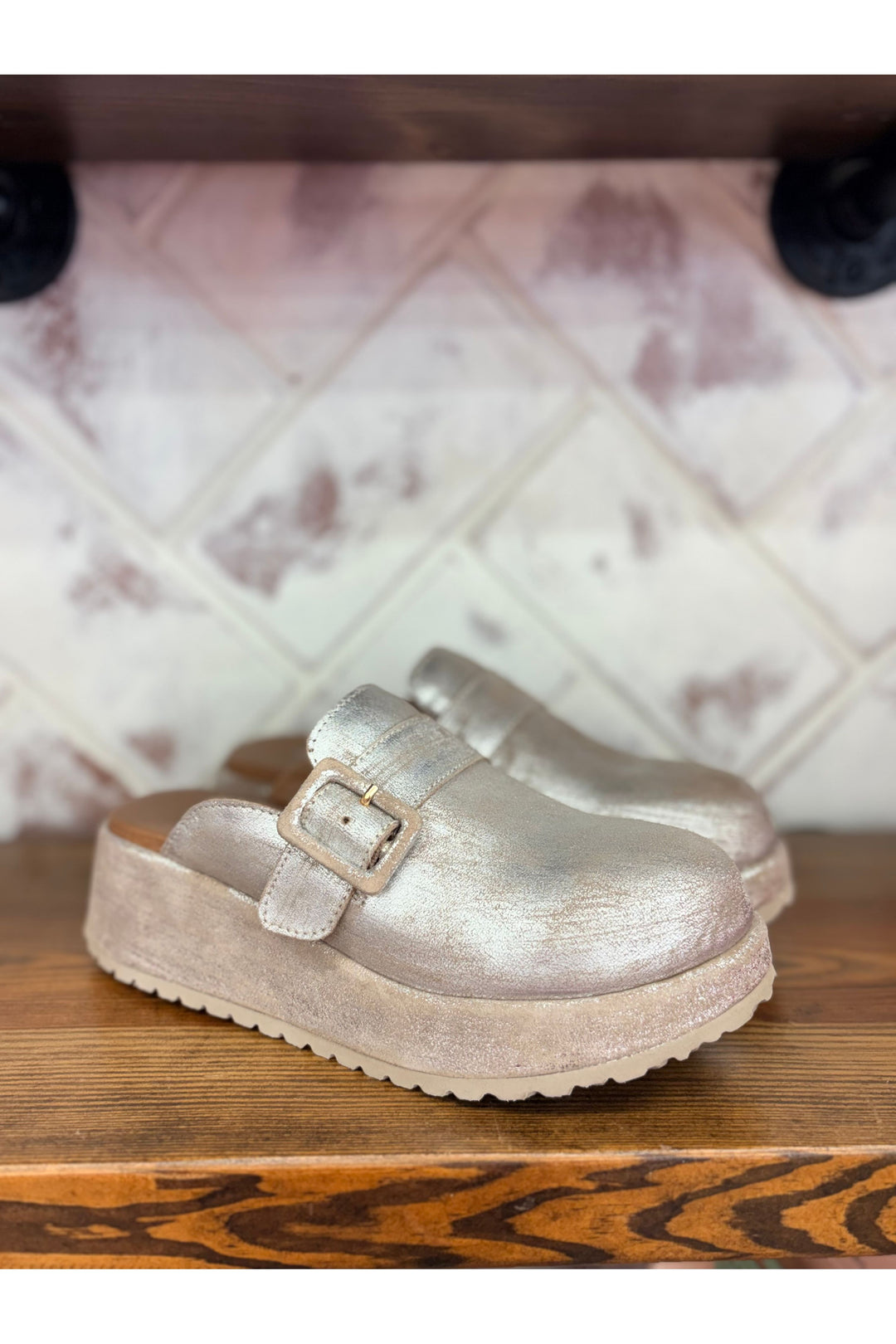 Silver clog shoe on a wooden surface with a tiled wall background
