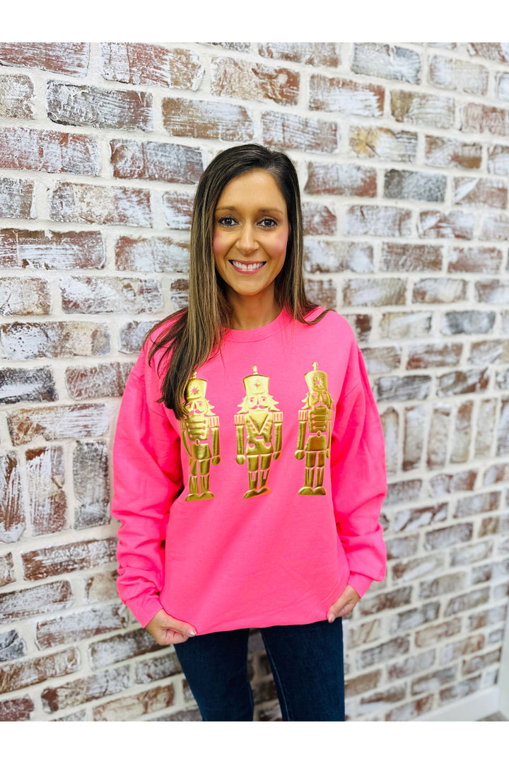 Person wearing a pink sweatshirt with gold graphic design against a brick wall.
