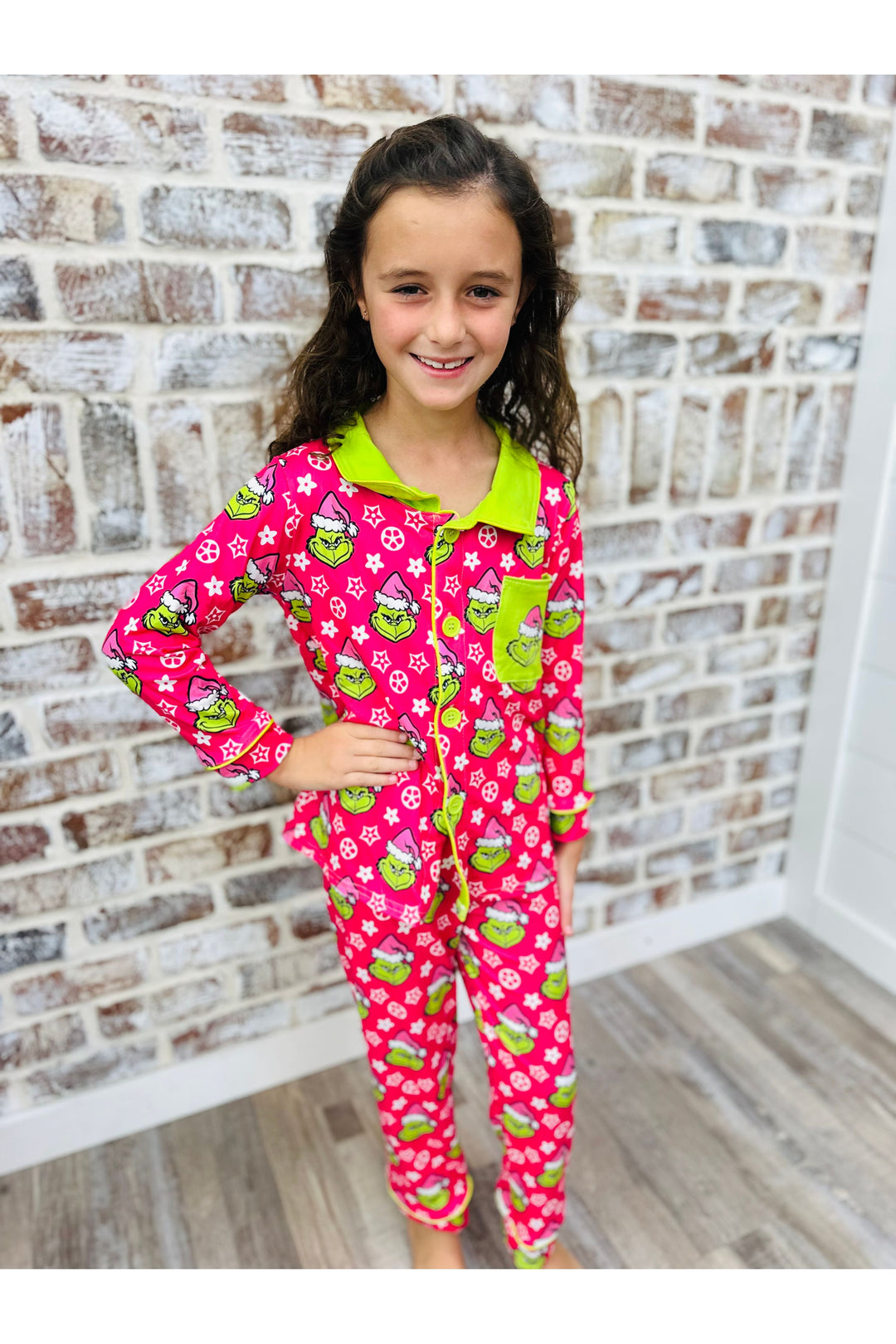 Young girl wearing pink pajamas with green accents against a brick wall.