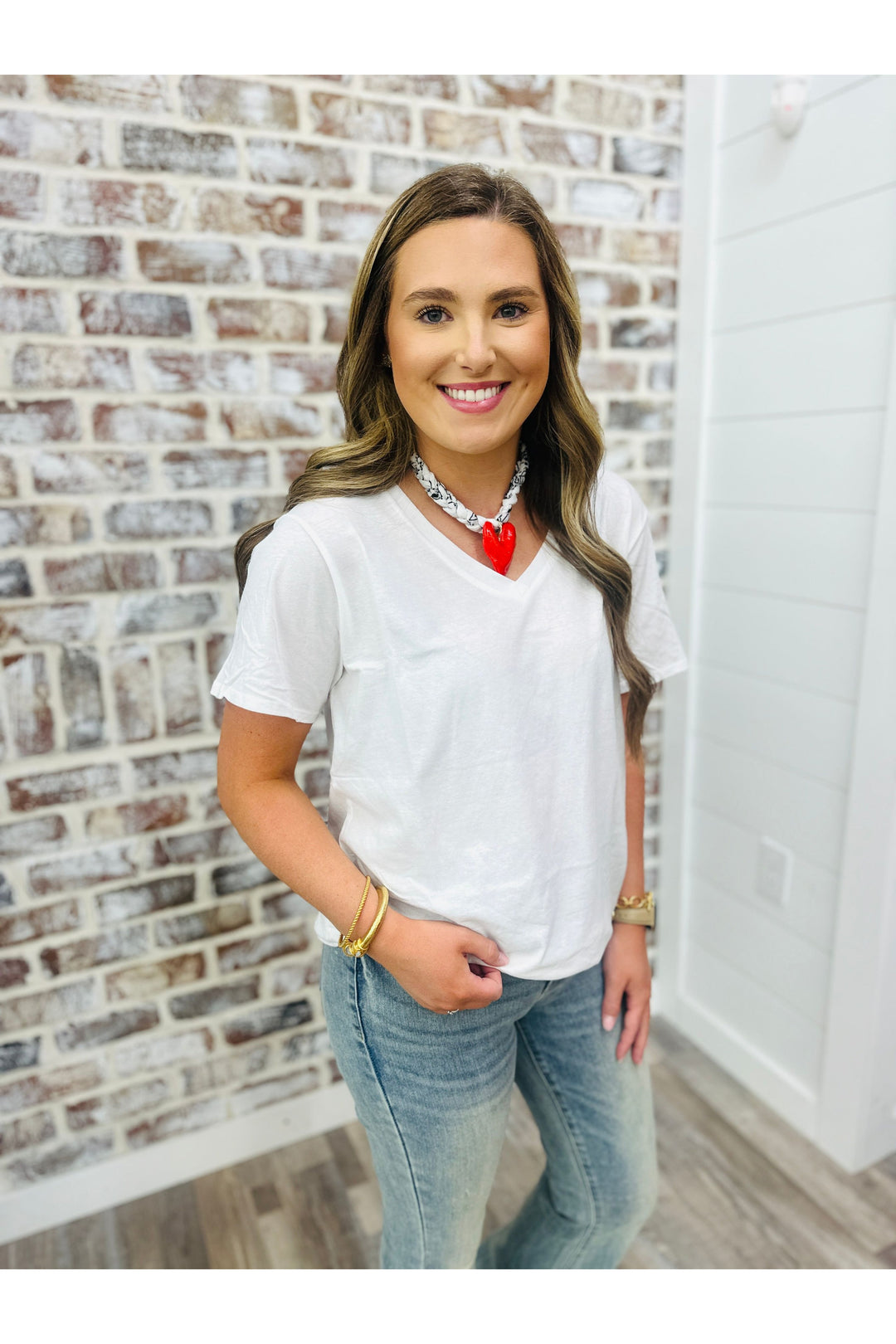 Woman wearing a solid white basic top standing against a brick wall.