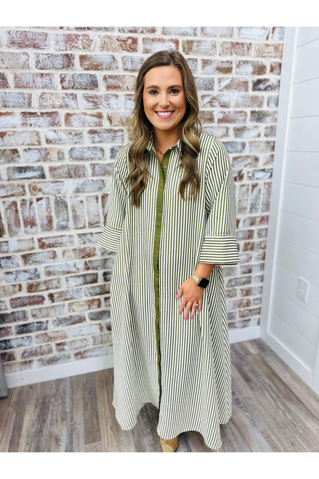 Woman wearing a long, striped dress standing in front of a brick wall.