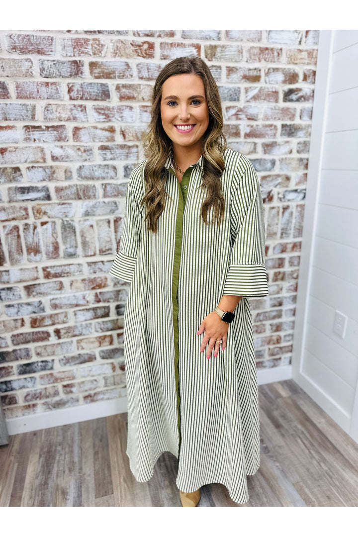 Woman wearing a long, striped dress standing in front of a brick wall.