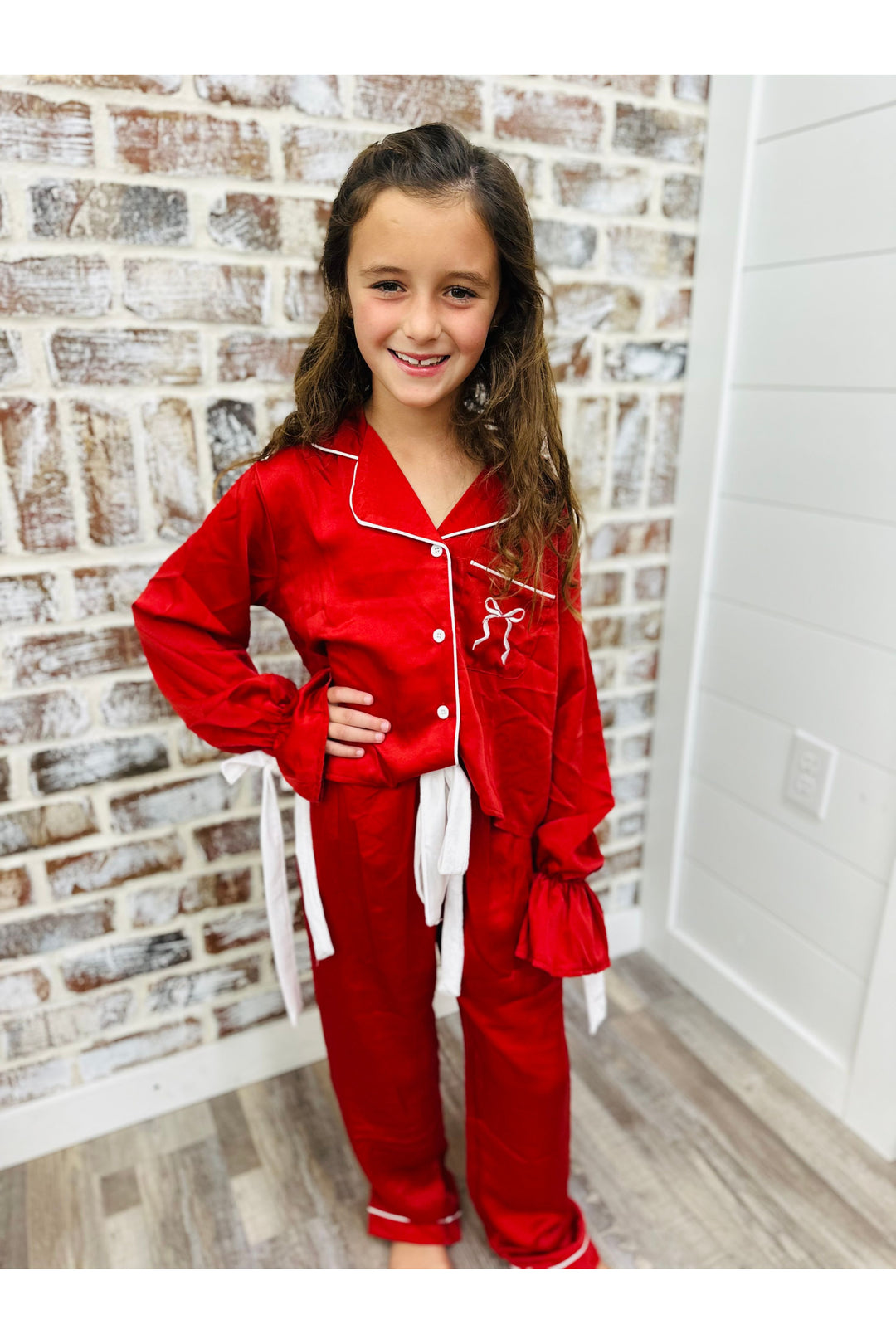 Young girl wearing red pajamas with a white logo against a brick wall.