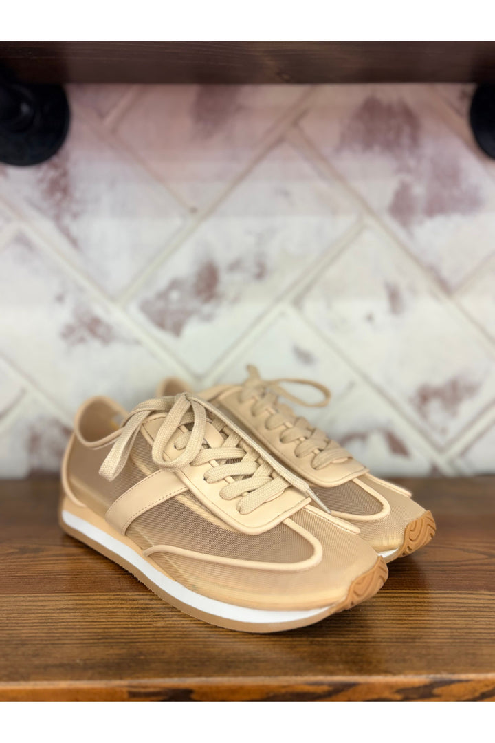 Beige sneakers on a wooden surface with a tiled wall background
