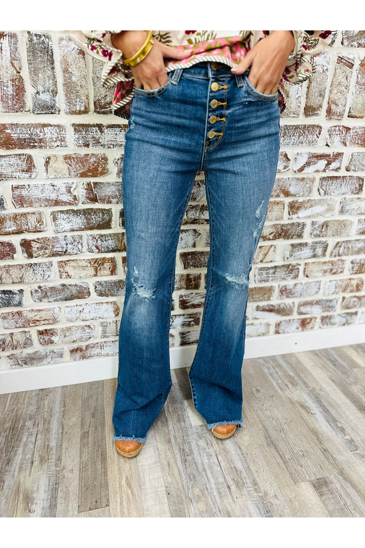 Person wearing blue flared jeans with decorative buttons against a brick wall.