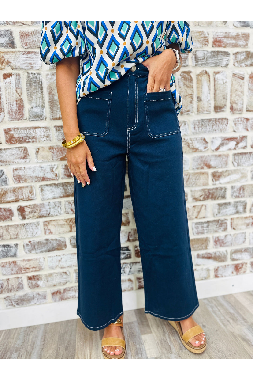 Woman wearing navy wide leg pants with white stitching standing against a brick wall.
