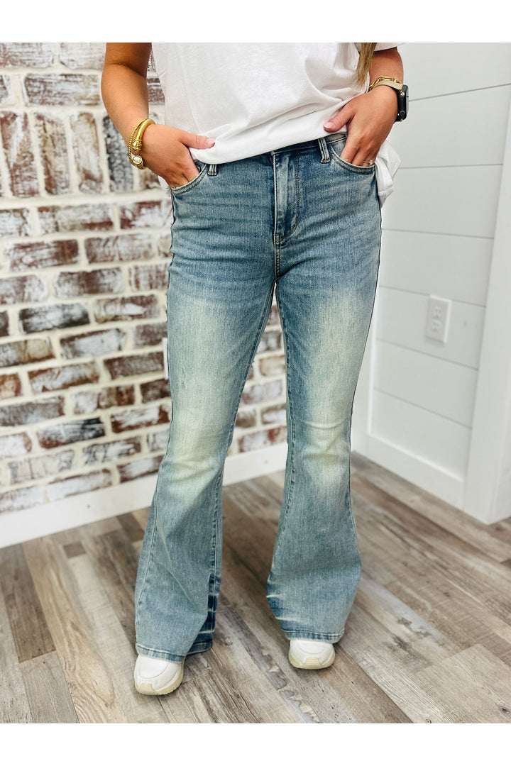 Woman wearing mid rise acid washed denim flares standing against a brick wall.