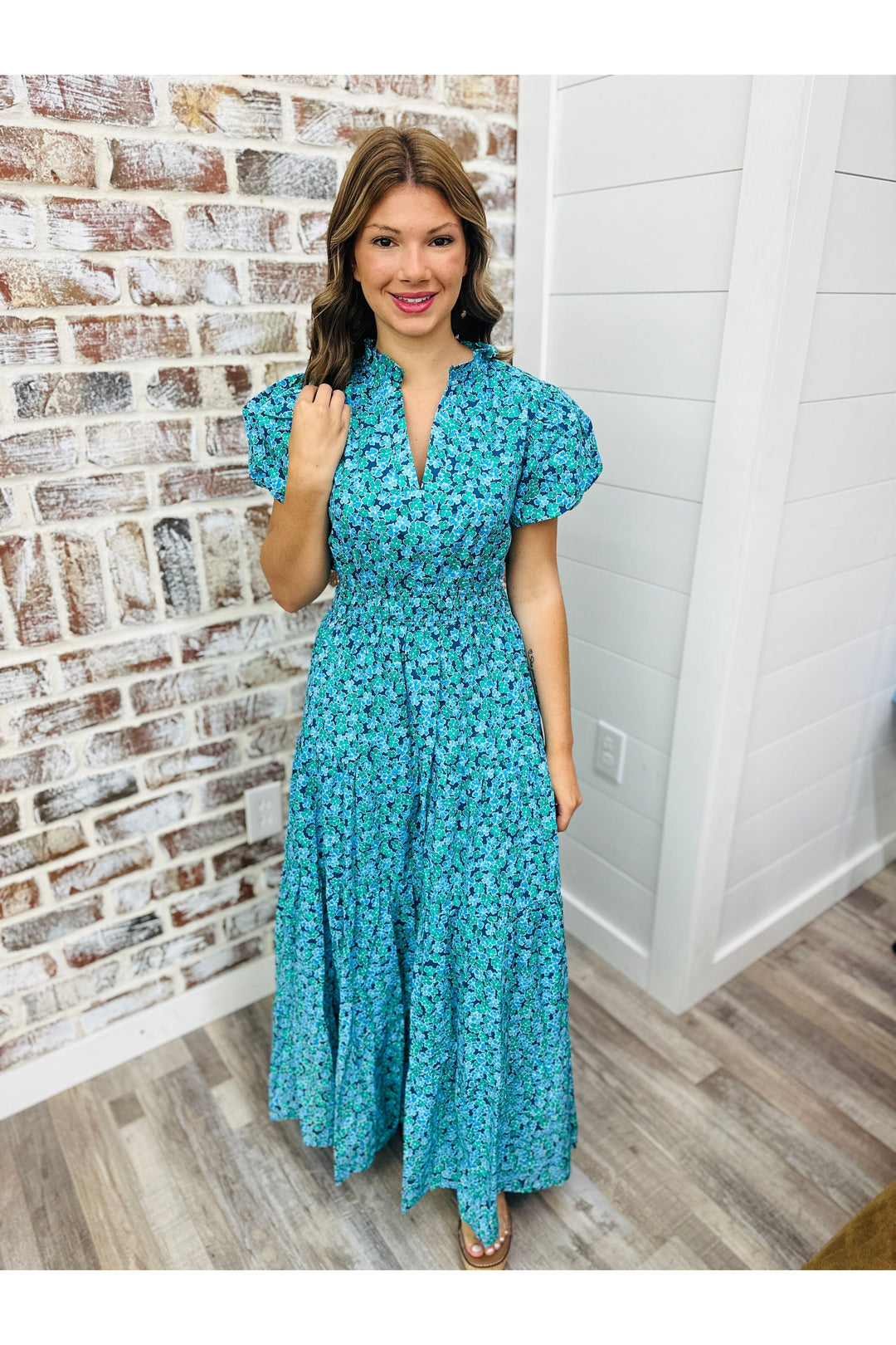 Woman wearing blue floral maxi dress standing against brick wall.