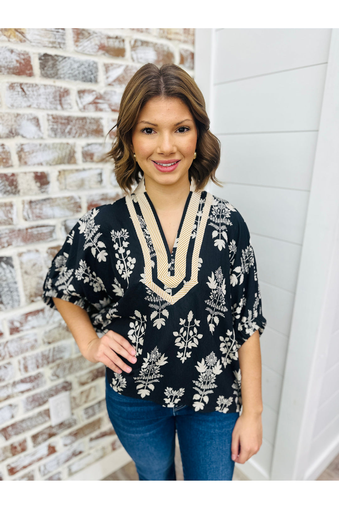 Woman wearing black top with tan floral detail and collar.