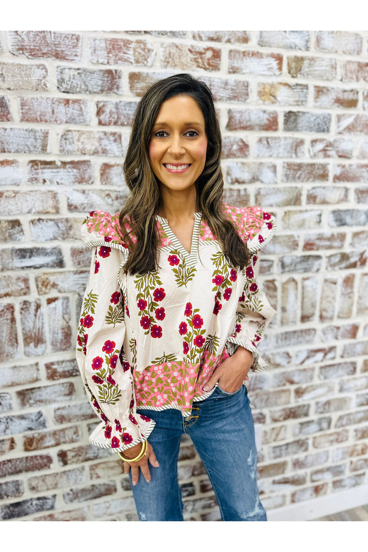 Woman wearing a floral blouse and jeans standing against a brick wall.