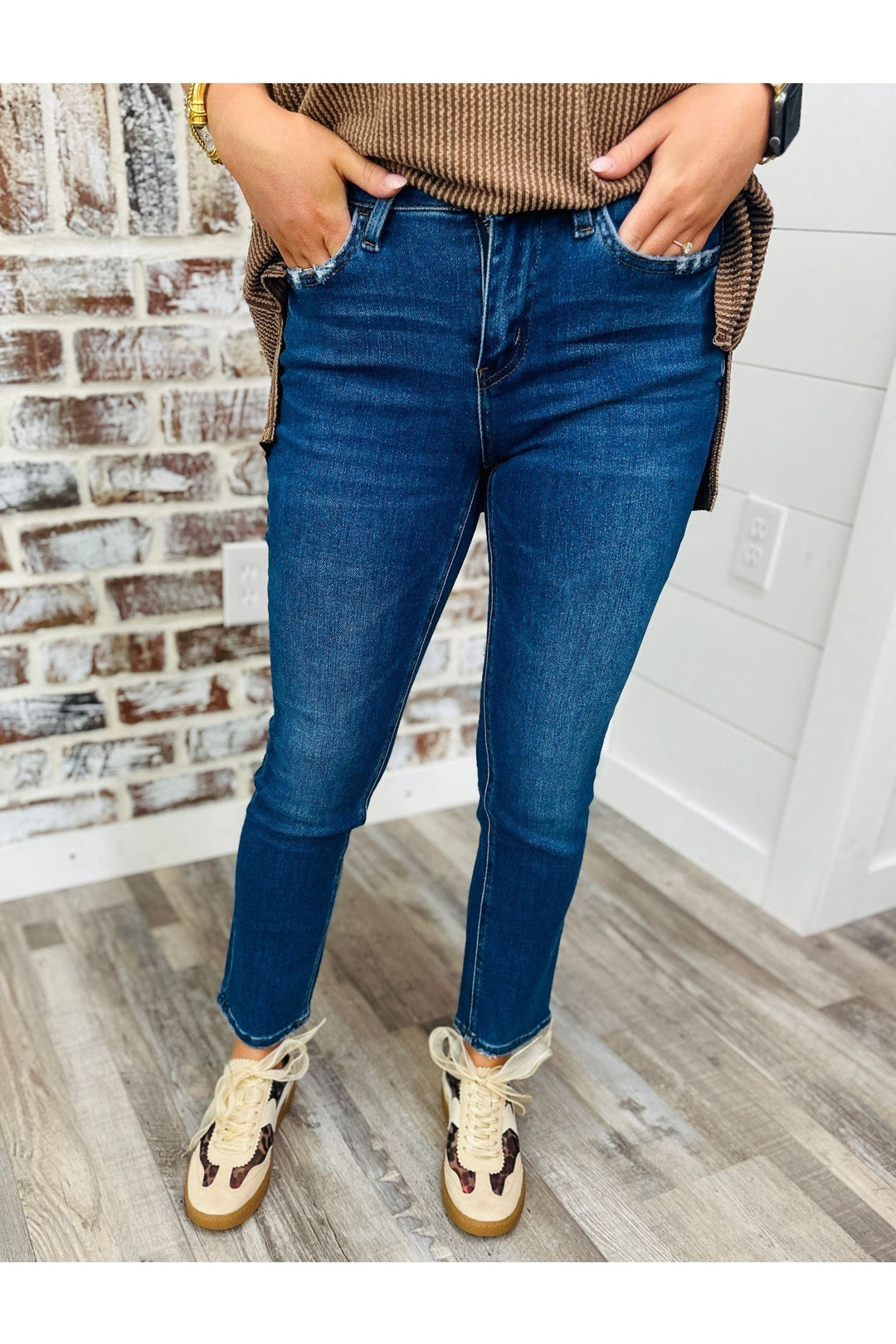 Woman wearing mid rise ankle slim straight jeans with tan and leopard sneakers standing against a brick wall. 