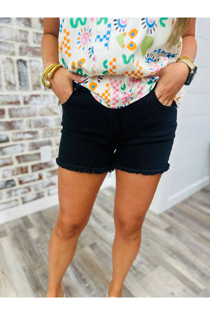 Woman wearing black shorts with frayed edges paired with a printed top.