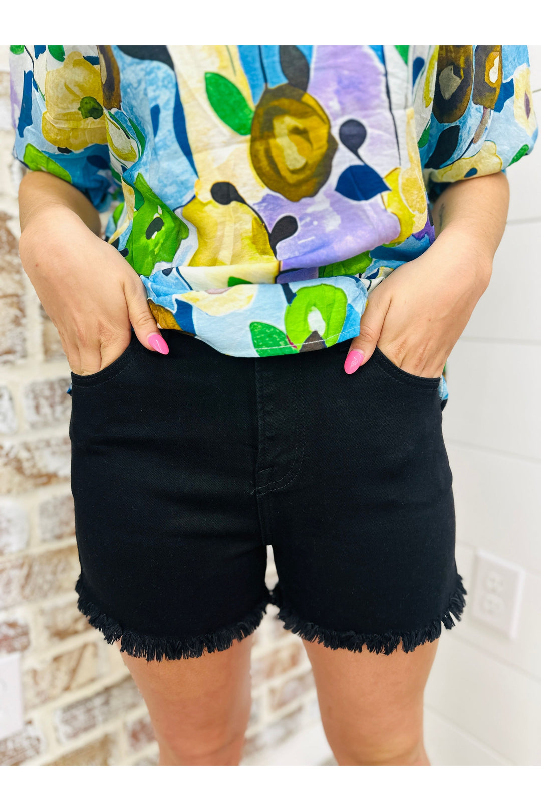 Woman wearing solid black high rise basic shorts with frayed hem paired with a pattern top.