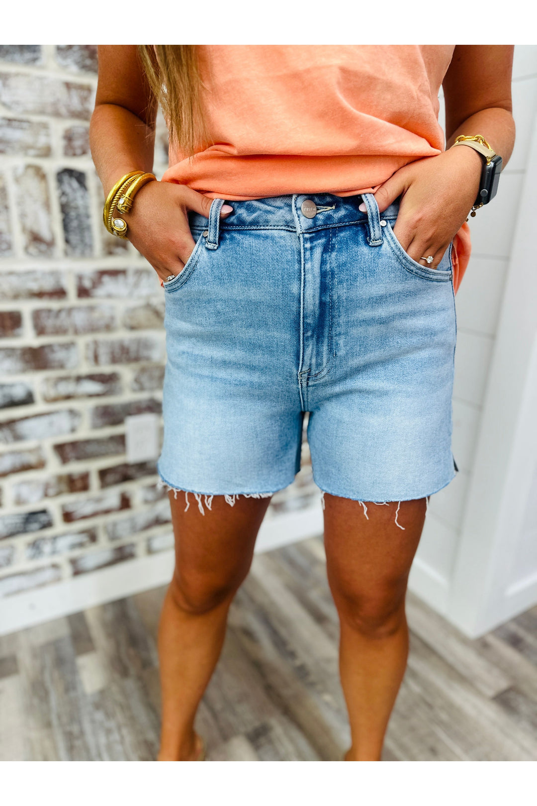 Woman wearing light wash denim shorts with a raw cut hem and small slits on the sides.