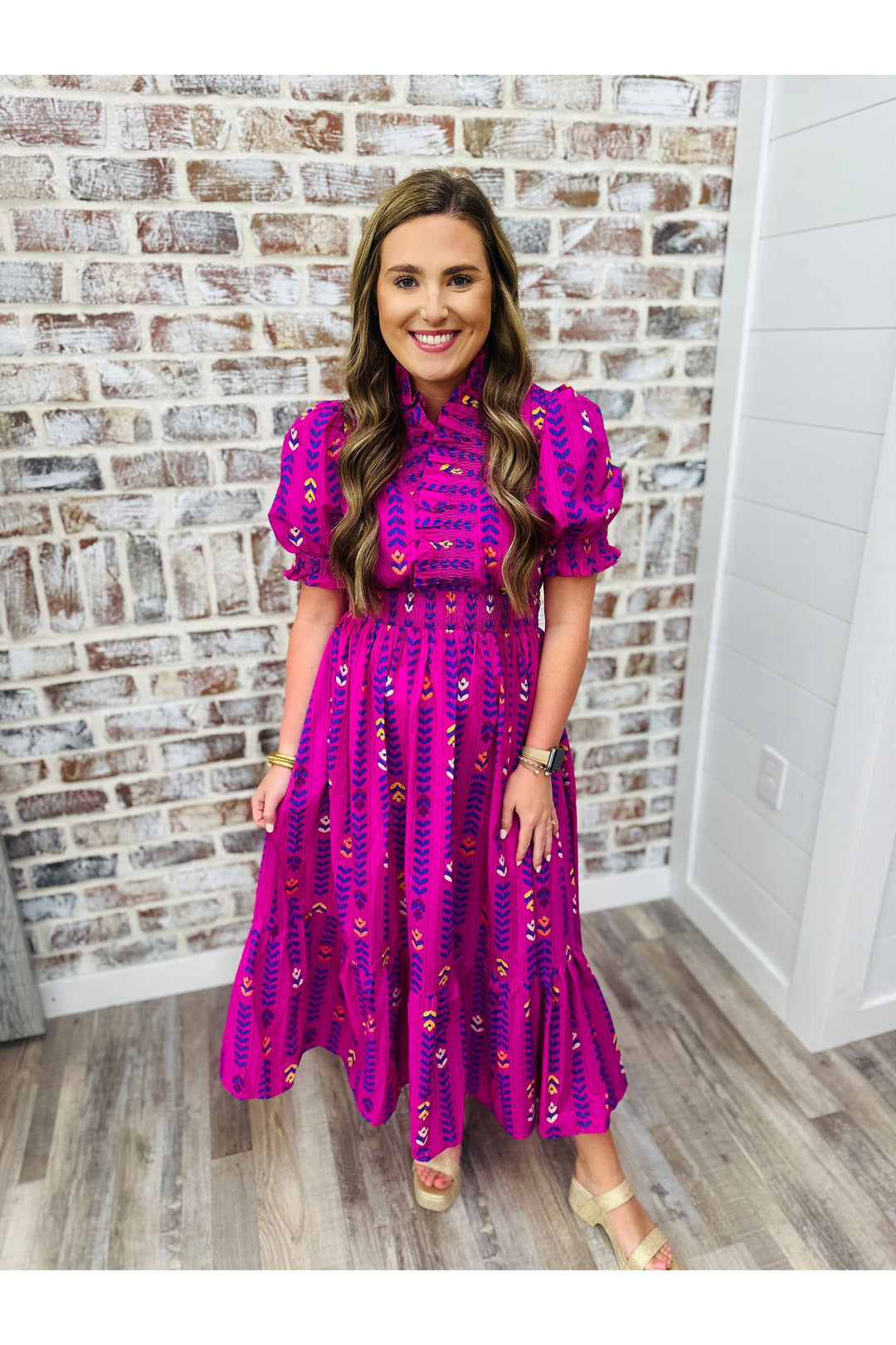 Woman wearing a magenta midi dress with floral detail and puff sleeves against a brick wall.