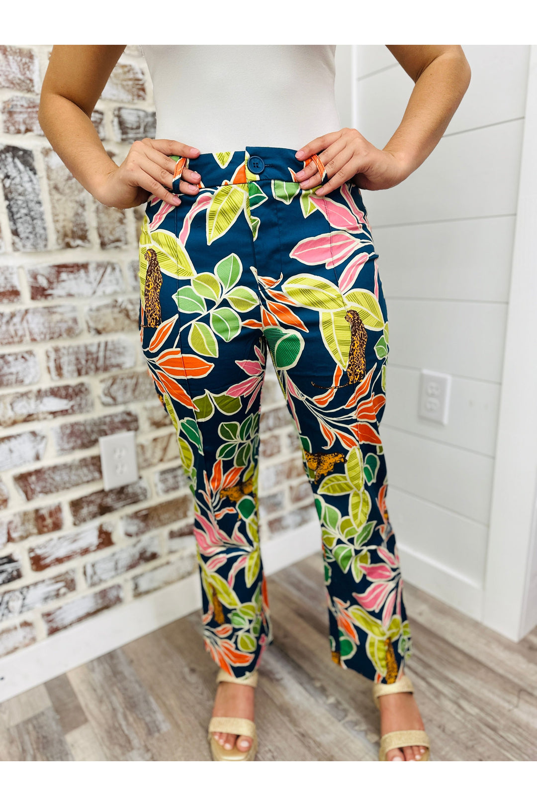 Woman wearing tropical printed pants standing against a brick wall.