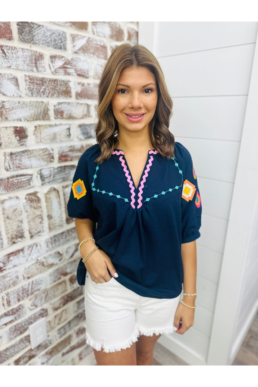 Woman wearing navy blue top with colorful embroidered detail on the sleeves paired with white shorts.