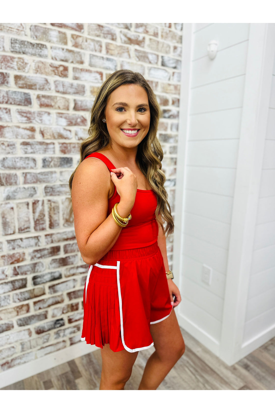 Woman wearing red athletic romper with white trim detail standing against a brick wall.
