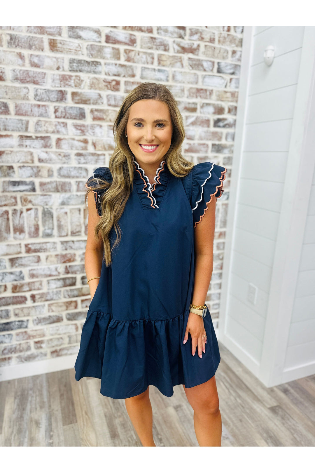 Woman wearing a navy dress with ric rac embroidery standing against a brick wall.
