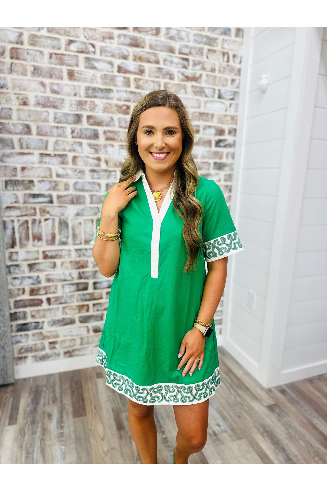 Woman wearing emerald green dress with white pattern detail around the bottom and sleeves. 