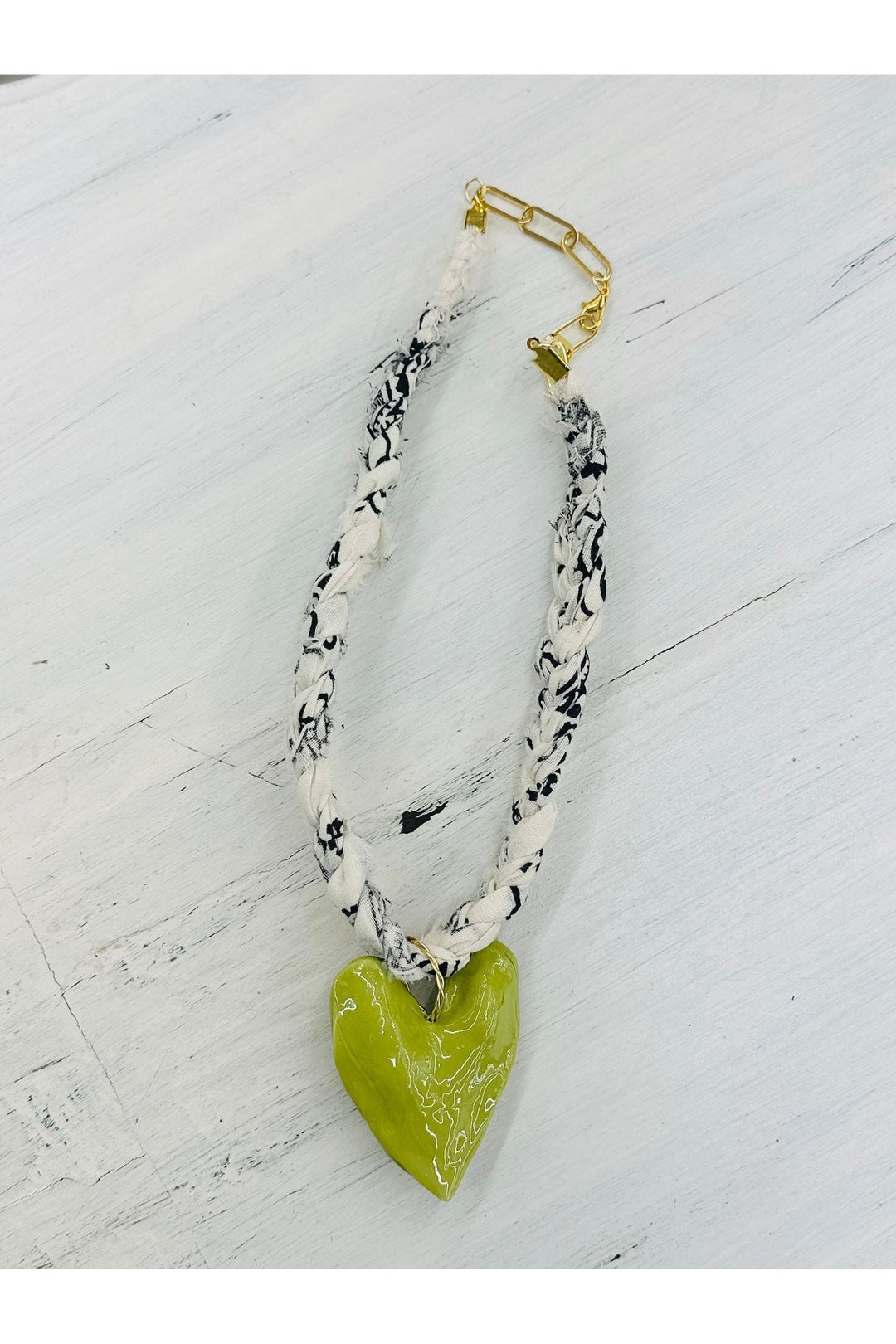 White and black braided scarf necklace with olive heart charm.