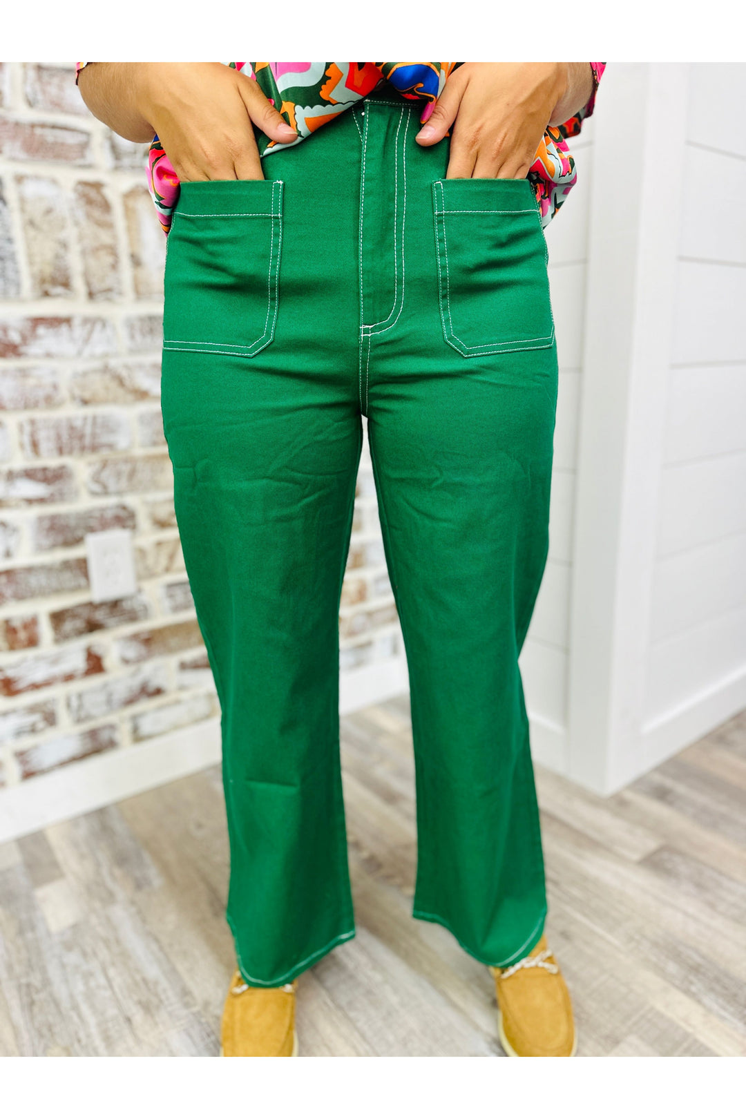 Woman wearing hunter green wide leg pants standing against a brick wall.