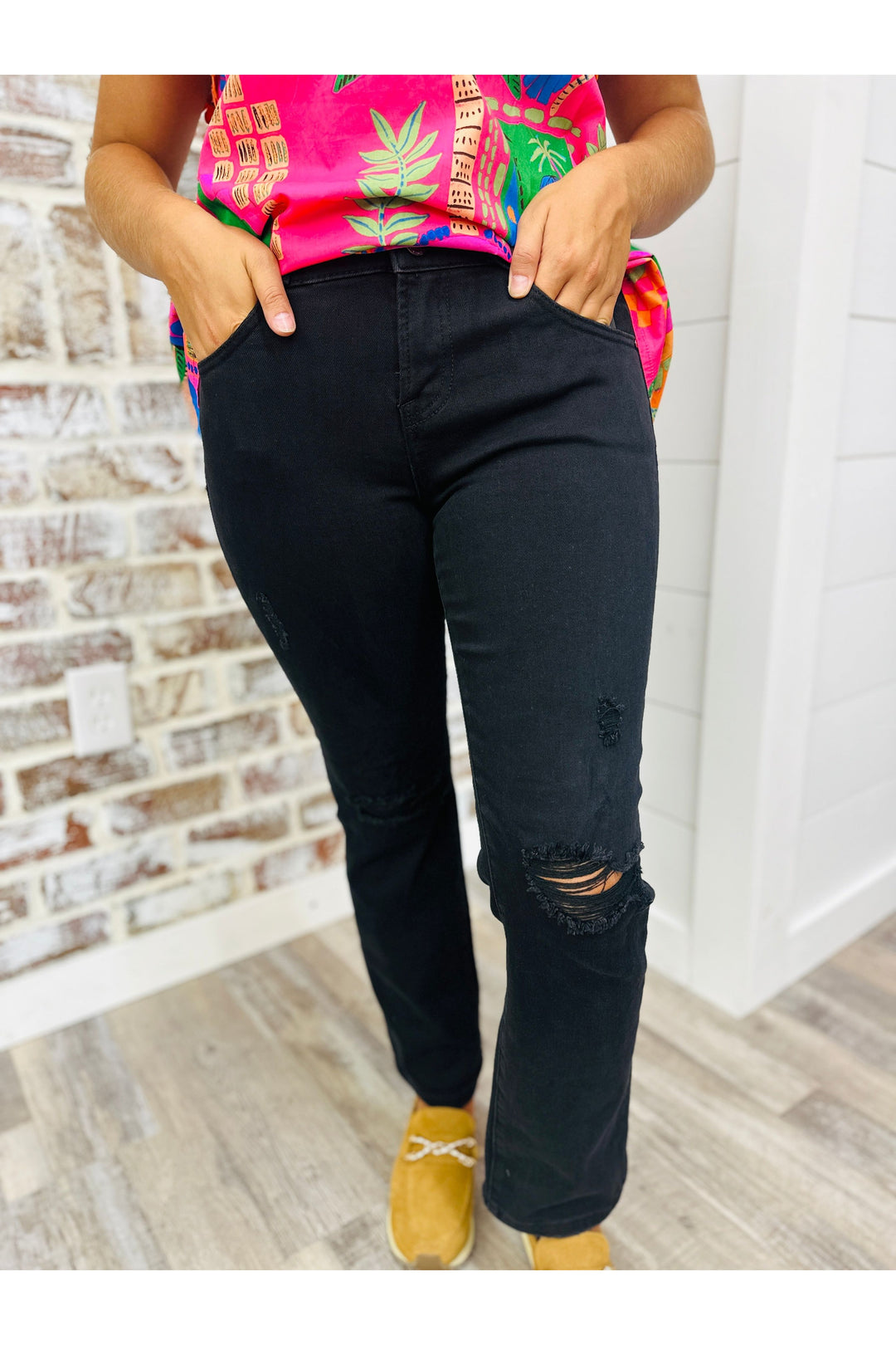 Woman wearing black denim jeans with distress in the knees standing against a brick wall.