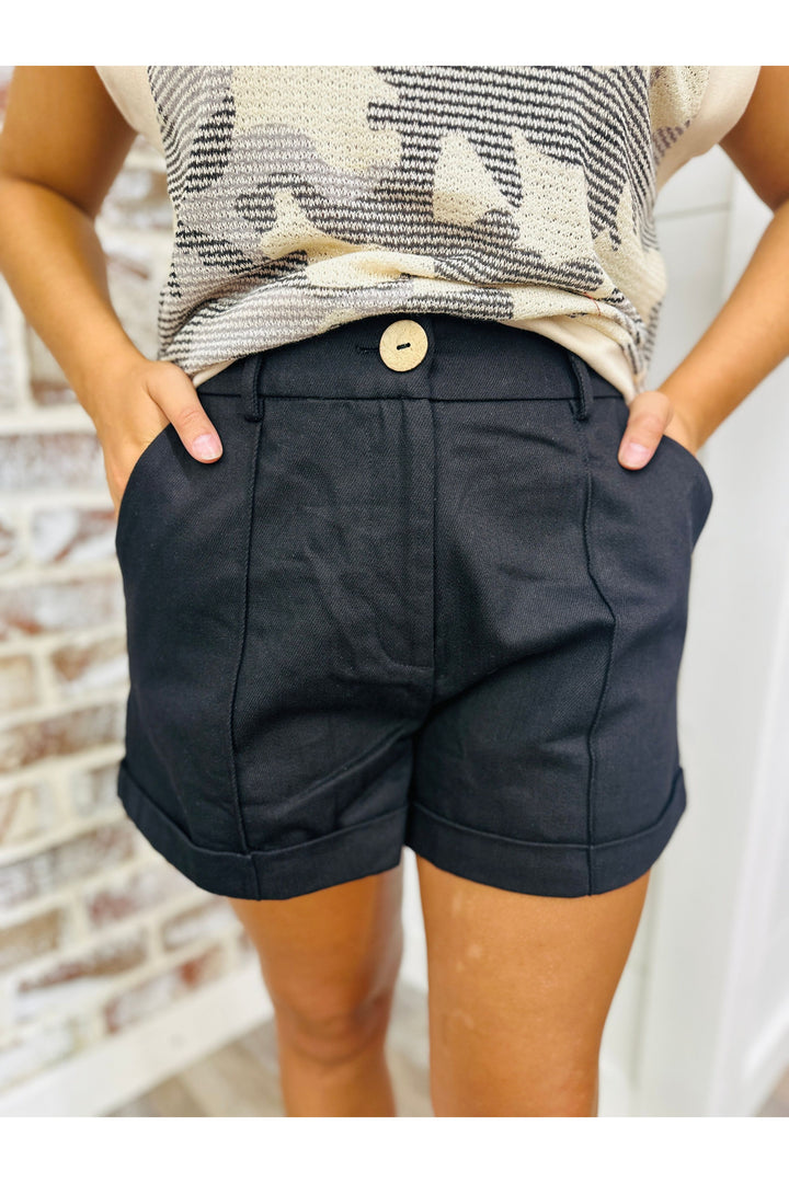 Woman wearing black pleated cuff shorts standing against a brick wall.