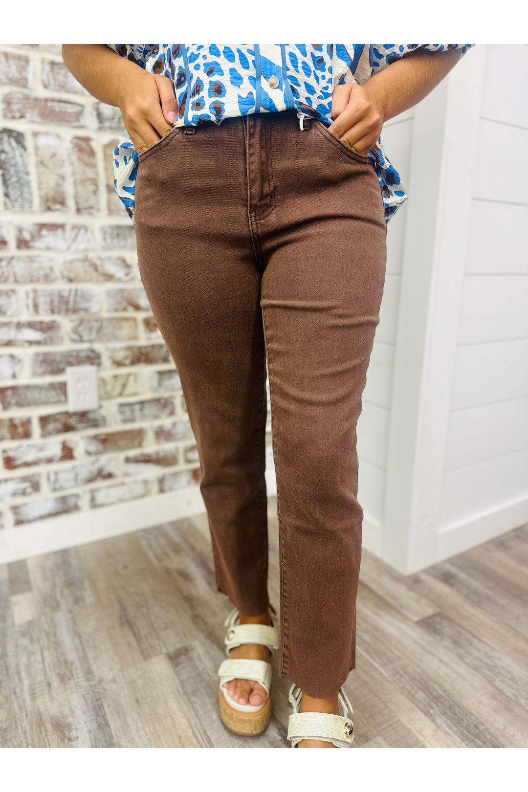Woman wearing brown pants paired with animal print top standing against a brick wall.