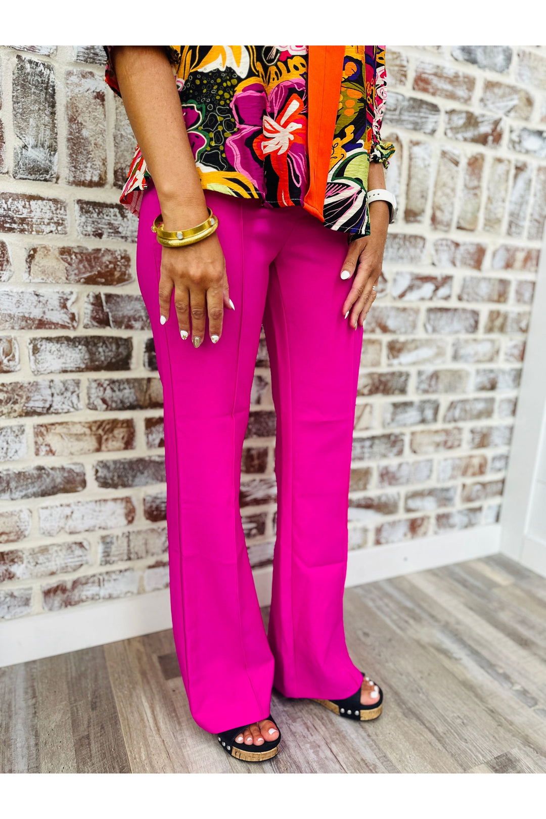 Woman wearing magenta flare dress pants standing against a brick wall.