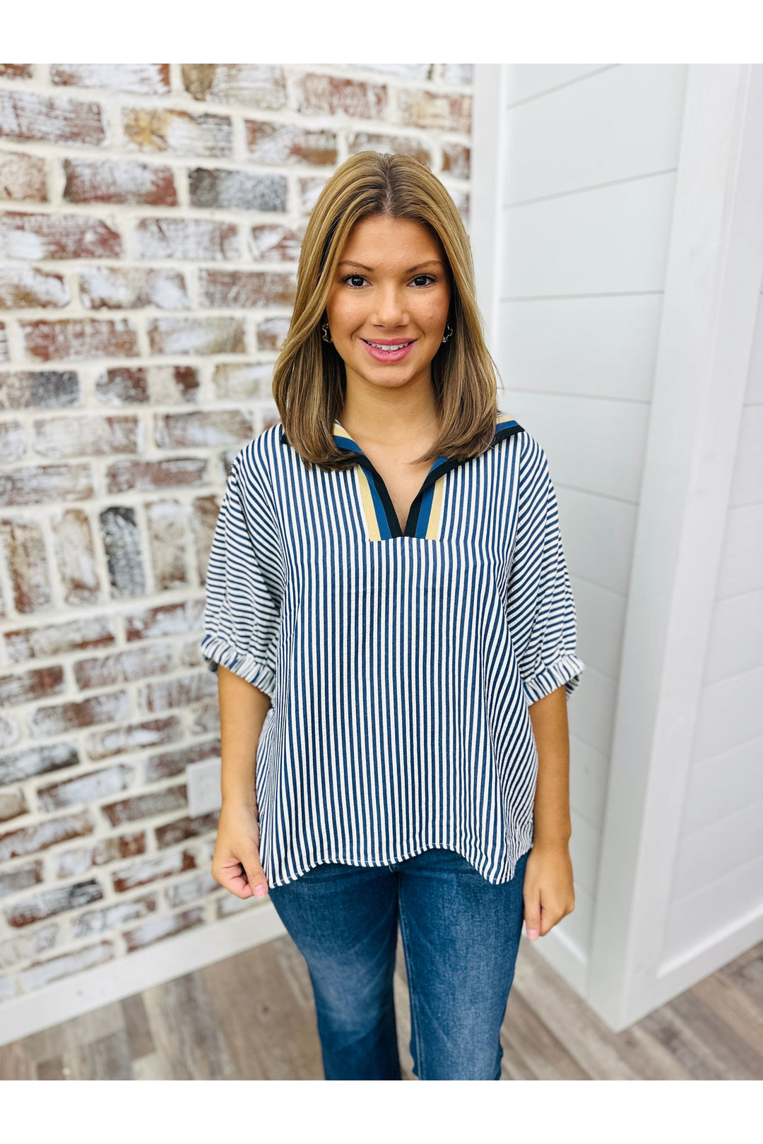 Woman wearing navy stripe top with collar detail standing against a brick wall.