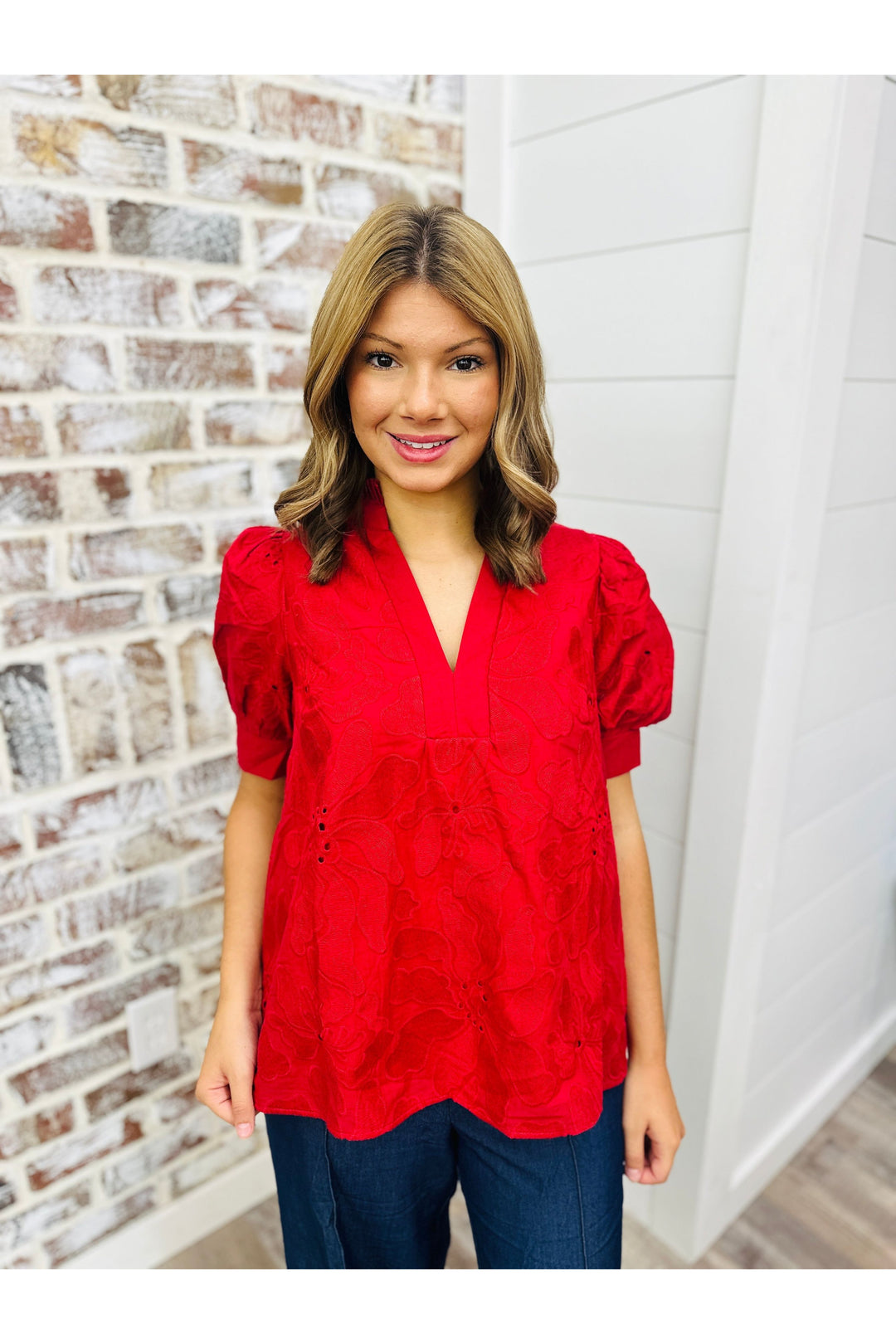 Woman wearing red puff sleeve top with floral lace detail.