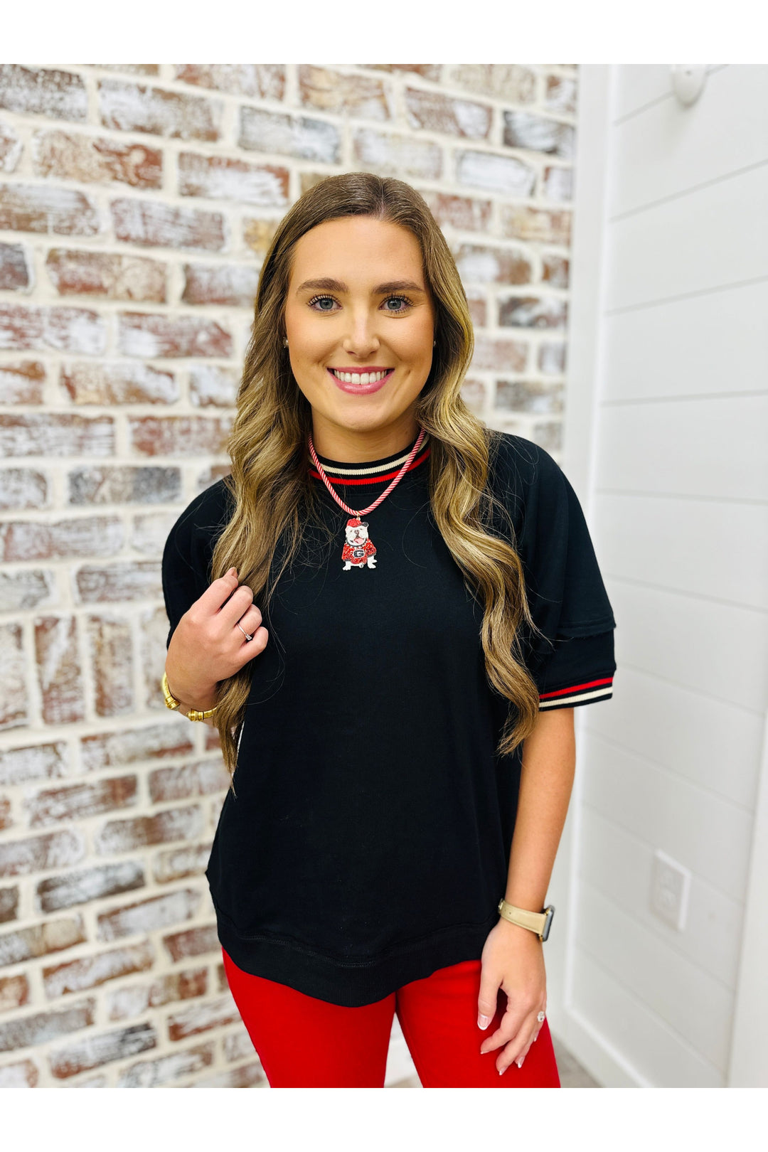 Woman wearing a black solid top with red and white stripe trim detail.
